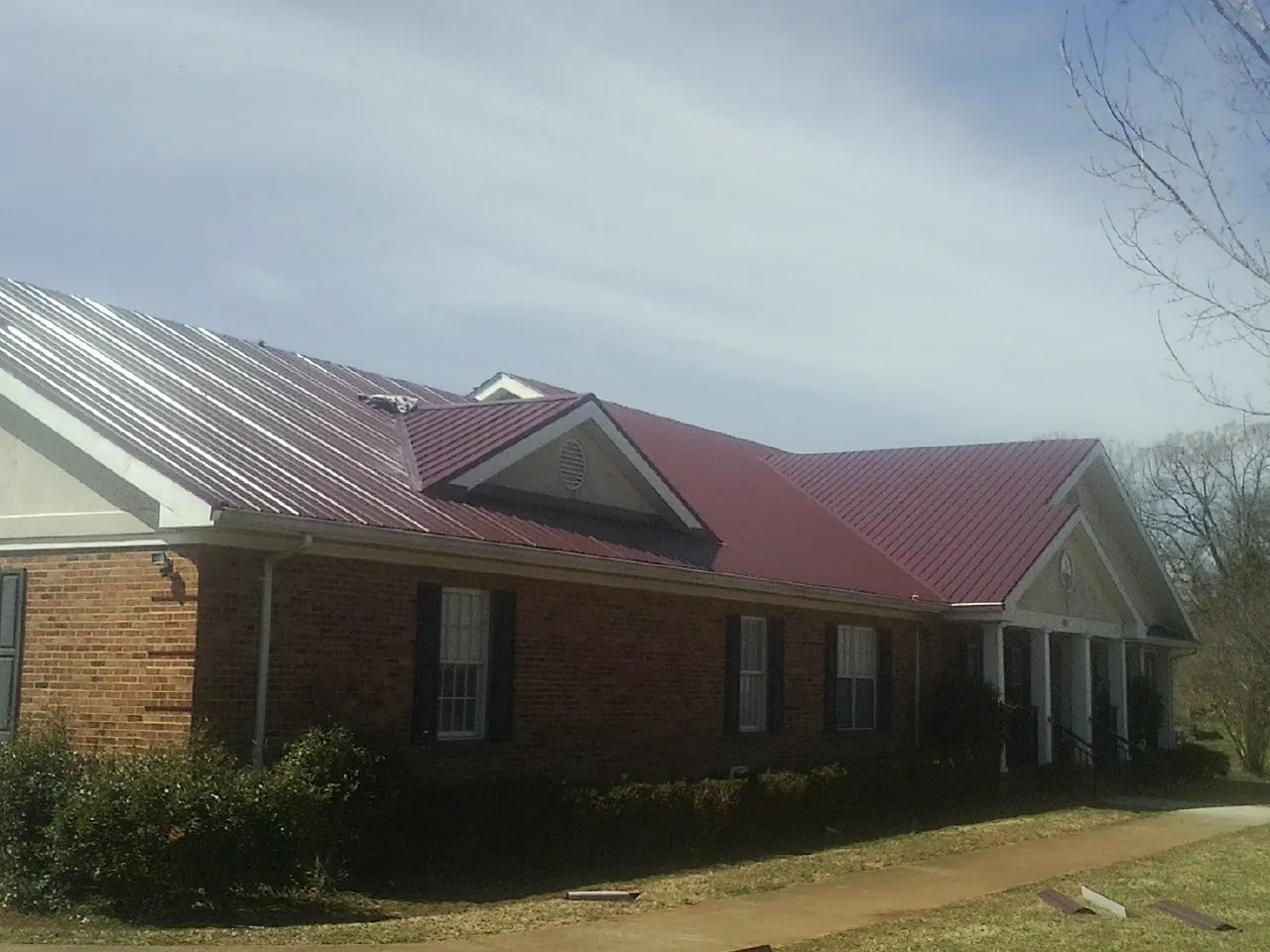 Red metal roof with gabled entries on a long brick building, from a Hail Damage Roof Repair job in Grays River