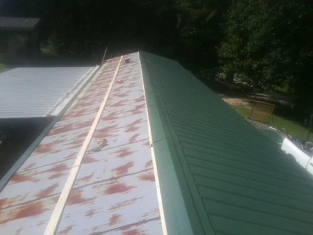 Old rusted panels beside newly installed green metal roofing — Wind Damage Roof Repair by Roofing Brothers in Grays River
