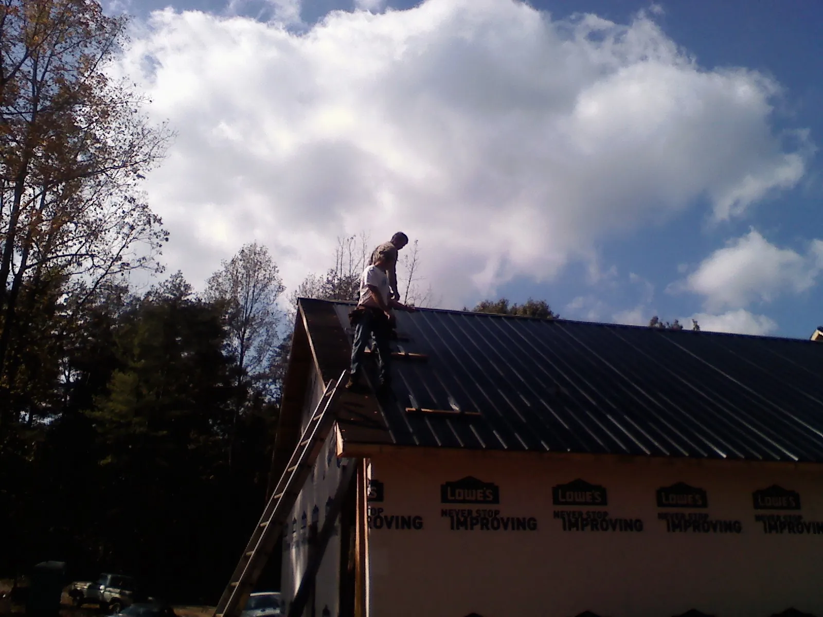 Roofer fastening dark metal panels high against a cloudy sky, from a Roof Inspection job in Grays River