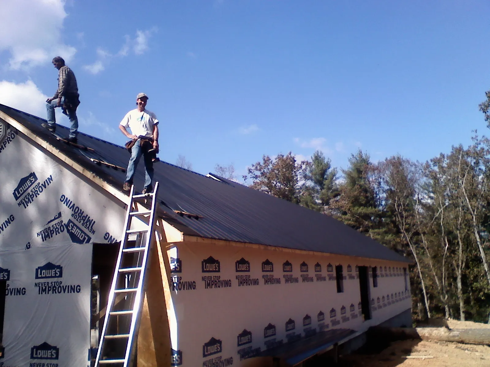 Two roofers standing on a long dark metal roof over a wrapped building in Grays River