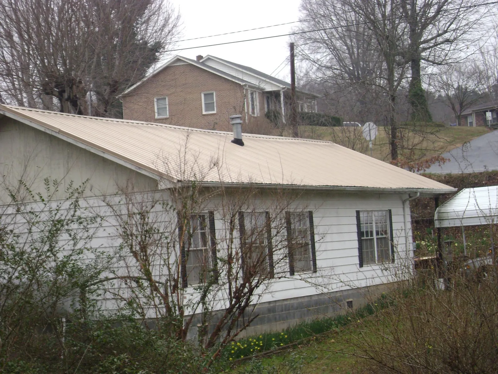 Tan metal roof on a white sided house set into a hillside — Commercial Roofing by Roofing Brothers in Grays River